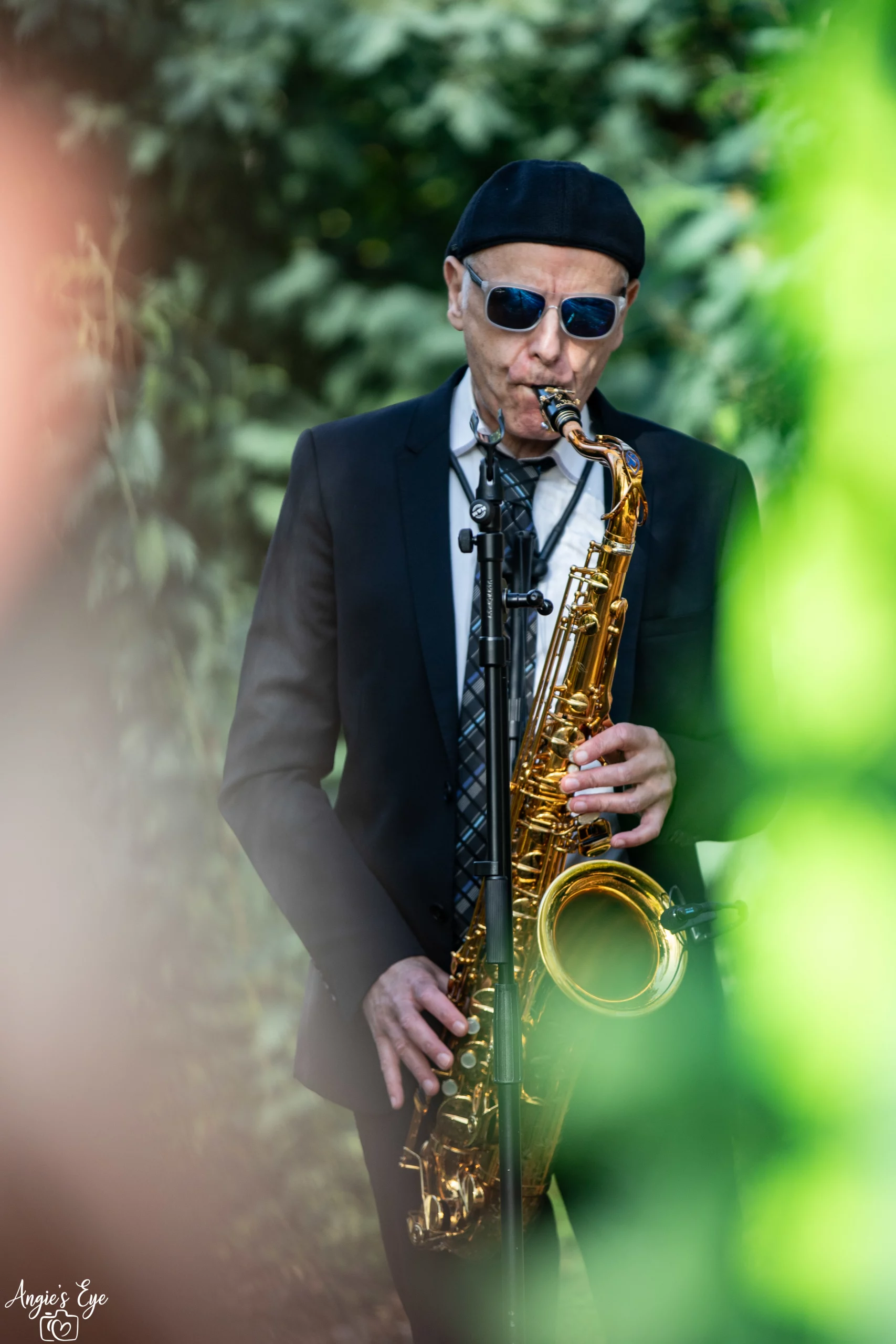 Saxophoniste stylé, costume/cravate/béret pour vous accompagner lors de votre cérémonie laïque ou pourquoi pas jusqu'à votre cocktail de mariage ? Cette photo prise parmi la végétation environnante ramène de la couleur, de la chaleur avec la lumière du soleil devinée sur ces feuilles verdoyantes